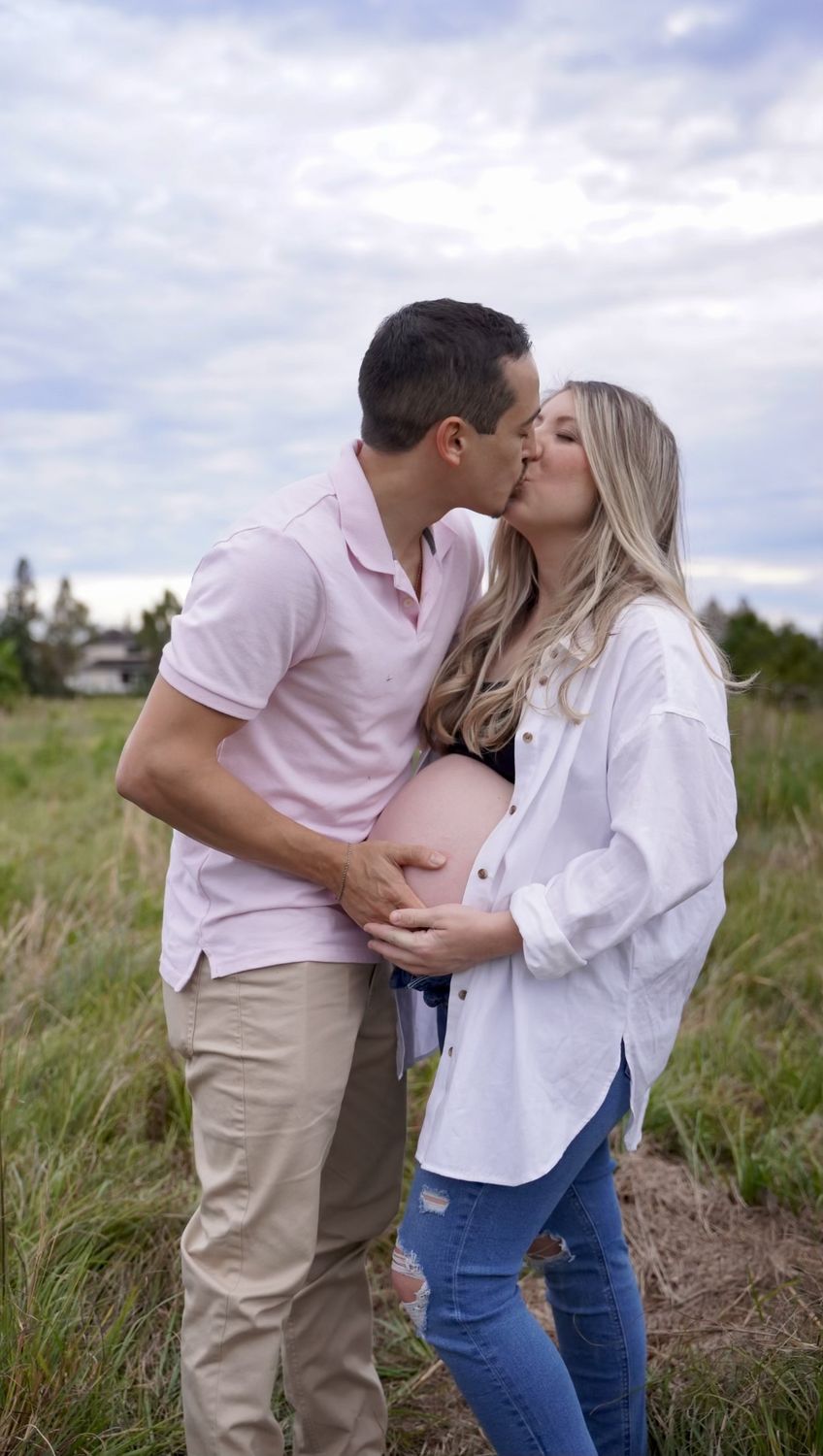 Expecting couple sharing a kiss in an open field